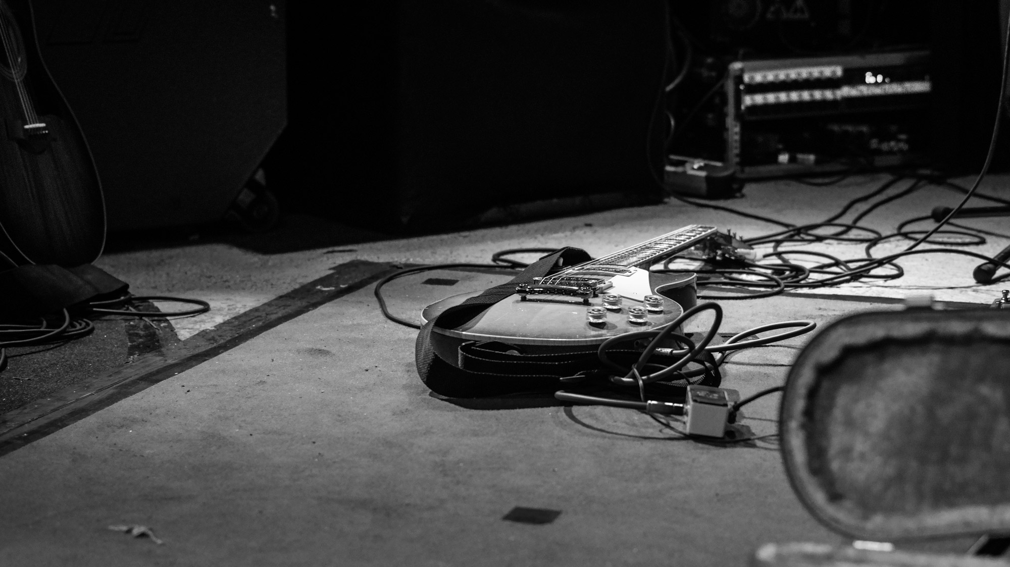 Escenario vacío de la sala Groove de Portugalete, en penumbra, poco antes del inicio del concierto de Hash; una guitarra eléctrica descansa horizontalmente en el suelo entre cables, pedales y pies de micro