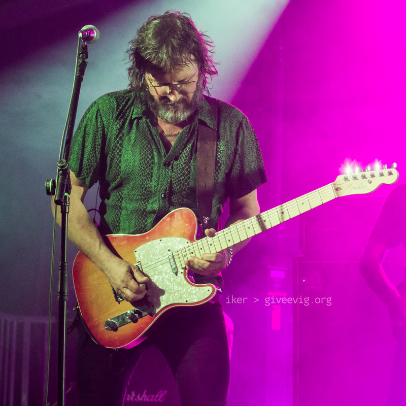 Gorka concentrado en su guitarra bajo potentes luces rosas.