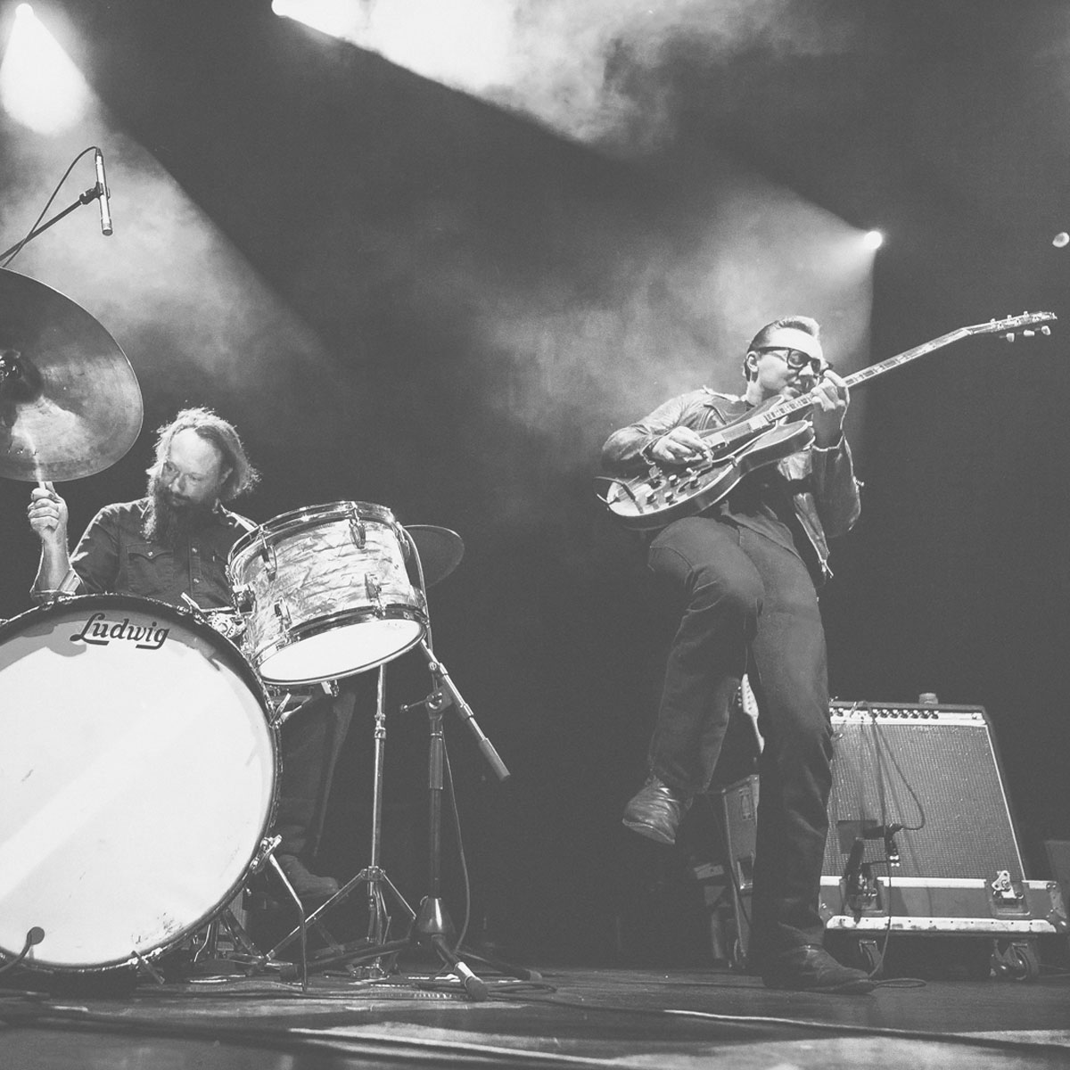 A la derecha McKinley James con su guitarra, haciendo un solo con gesto de esfuerzo y disfrute y la pierna levantada. A la izquierda, su baterista y padre, Jason Smay, en una batería Ludwig