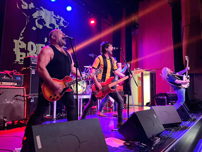 Miembros de Porco Bravo haciendo coros bajo líneas de luz de los focos